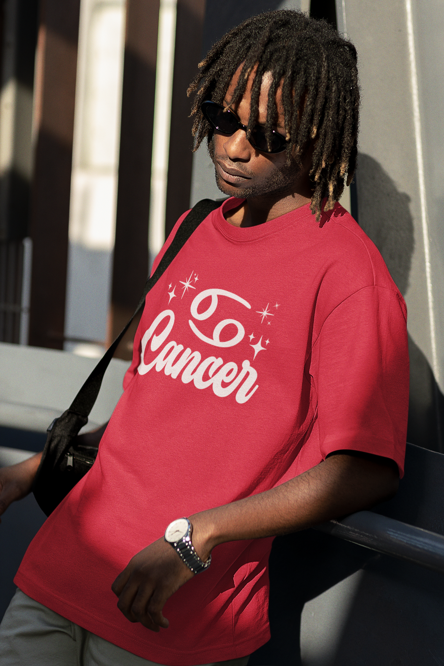 Person wearing a red t-shirt with 'Cancer' white text design, standing against a building.