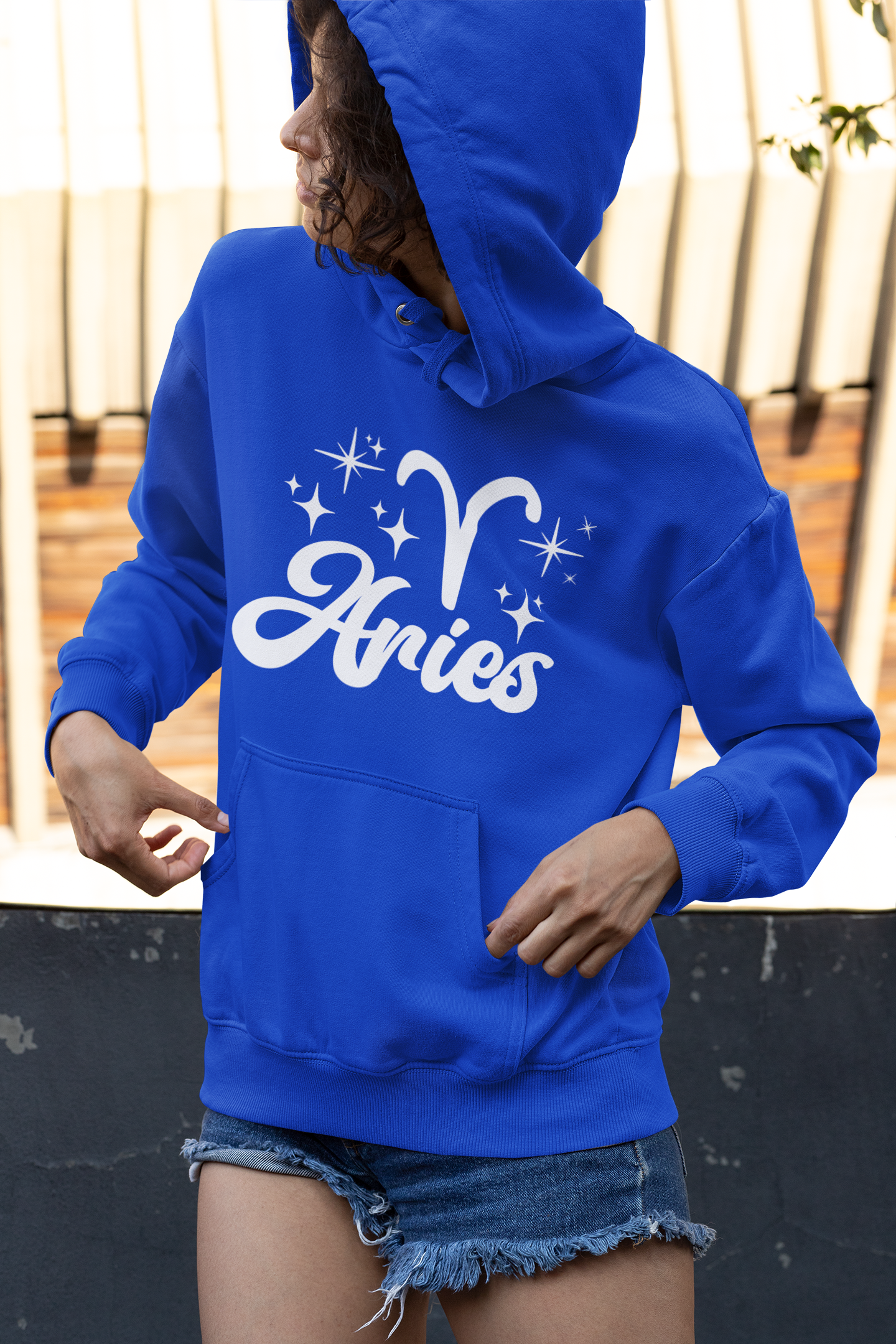 Person wearing a blue hoodie with 'Aries with zodiac symbol' white text, standing outdoors.