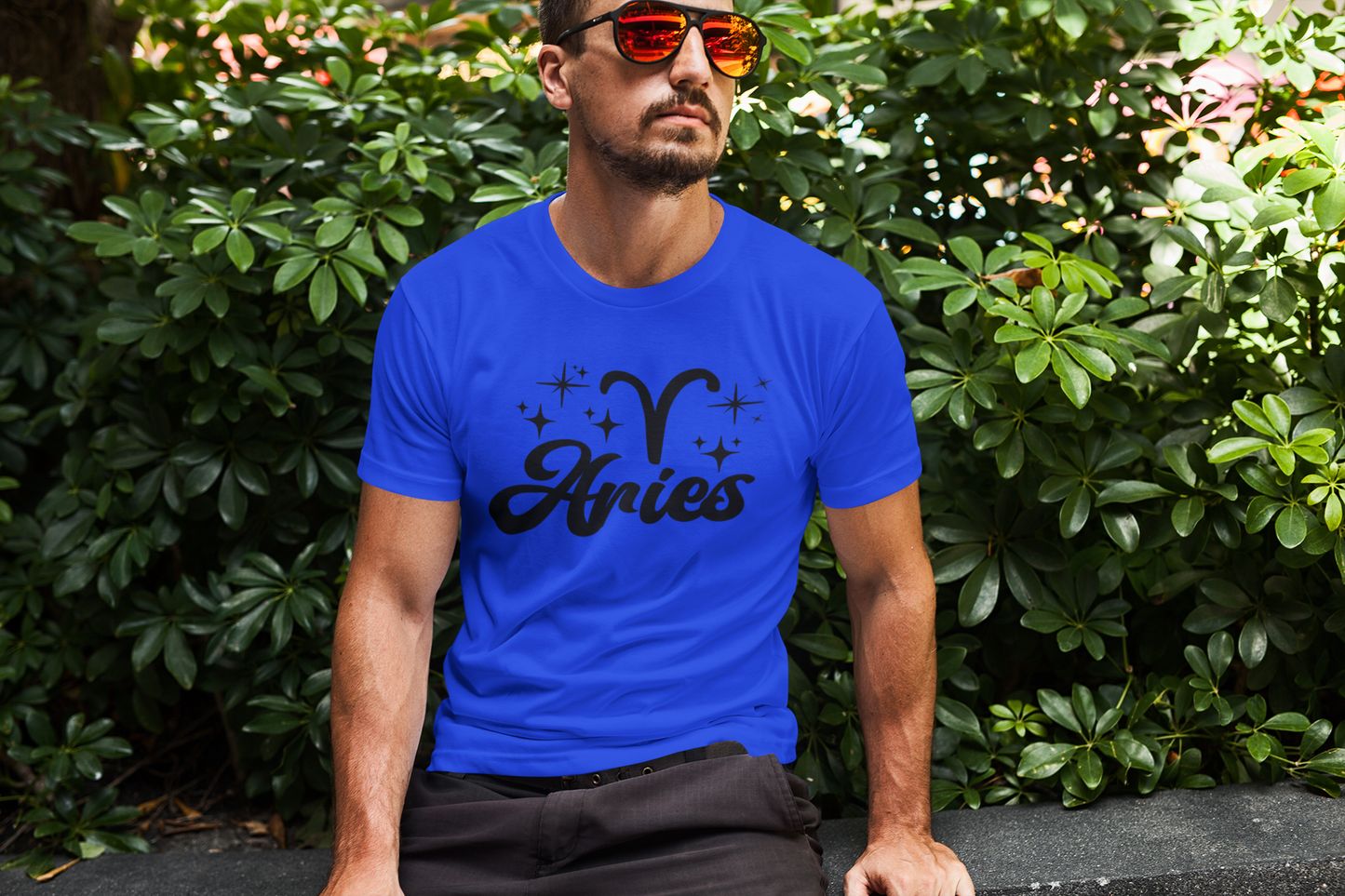 Man wearing an blue t-shirt with 'Aries' black text design sitting outdoors.