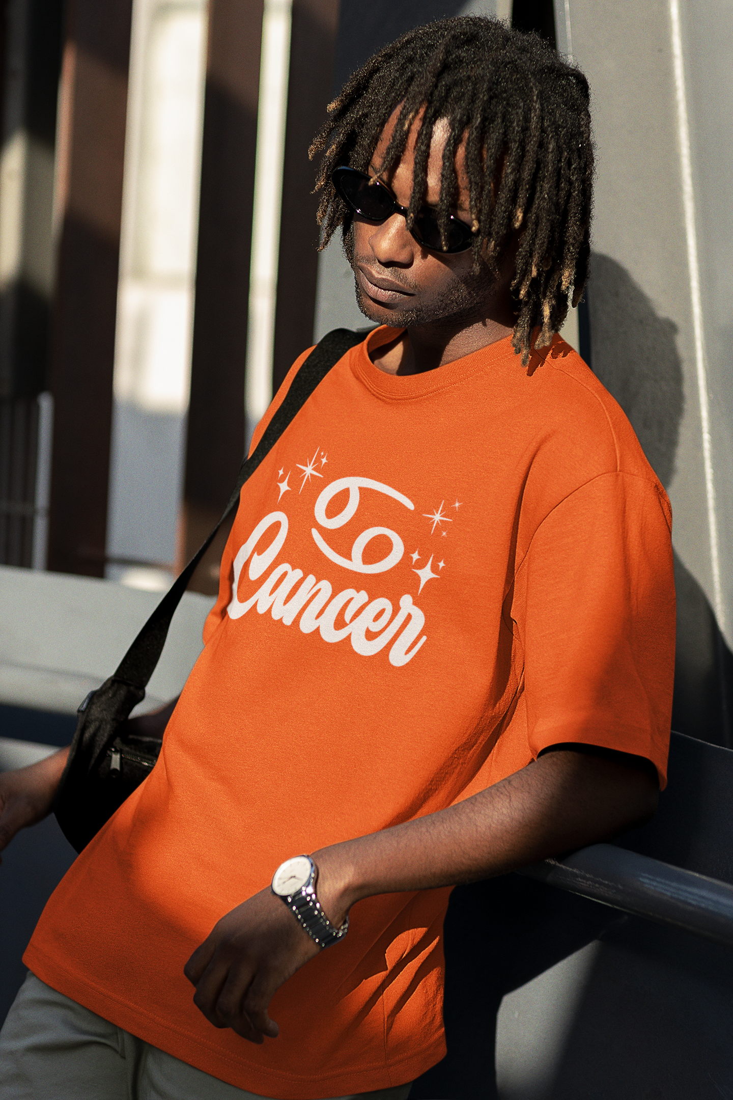 Person wearing a orange t-shirt with 'Cancer' white text design, standing against a building.