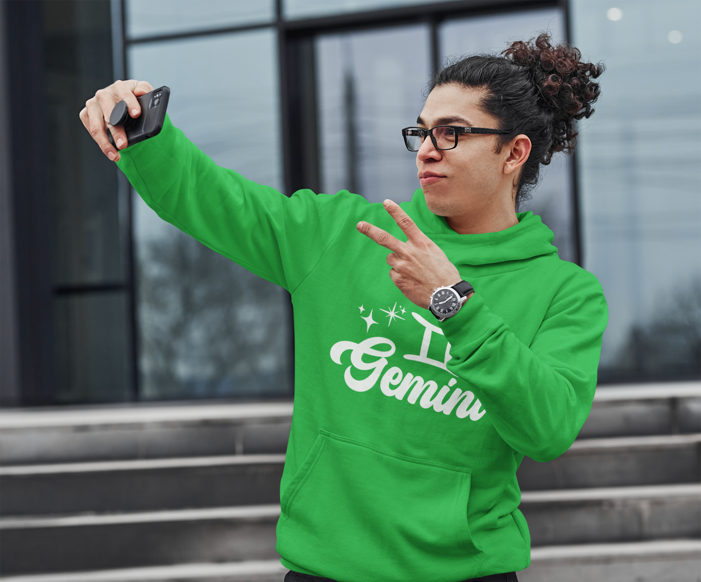 Person wearing an green hoodie with 'Gemini' white text, taking a selfie outdoors.
