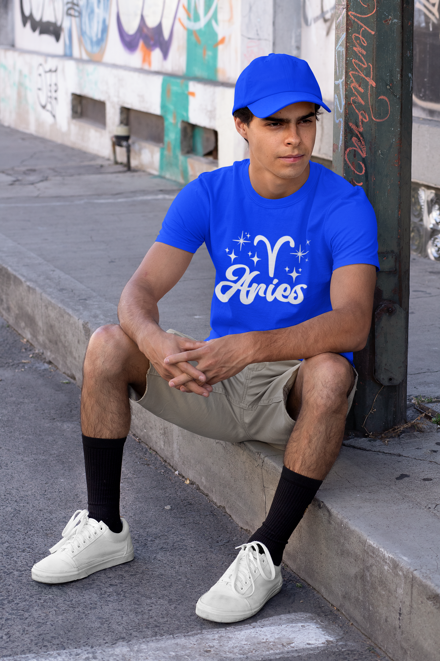 Person wearing a blue 'Aries' white text design t-shirt sitting on a sidewalk.