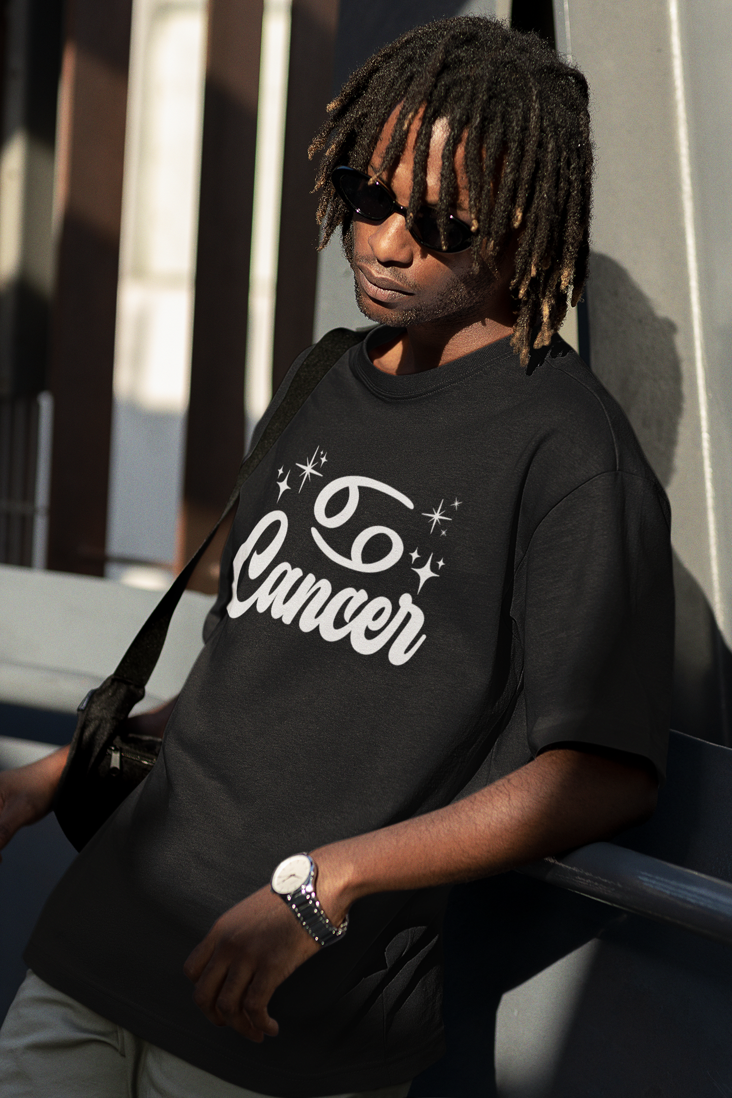 Person wearing a black t-shirt with 'Cancer' white text design, standing against a building.