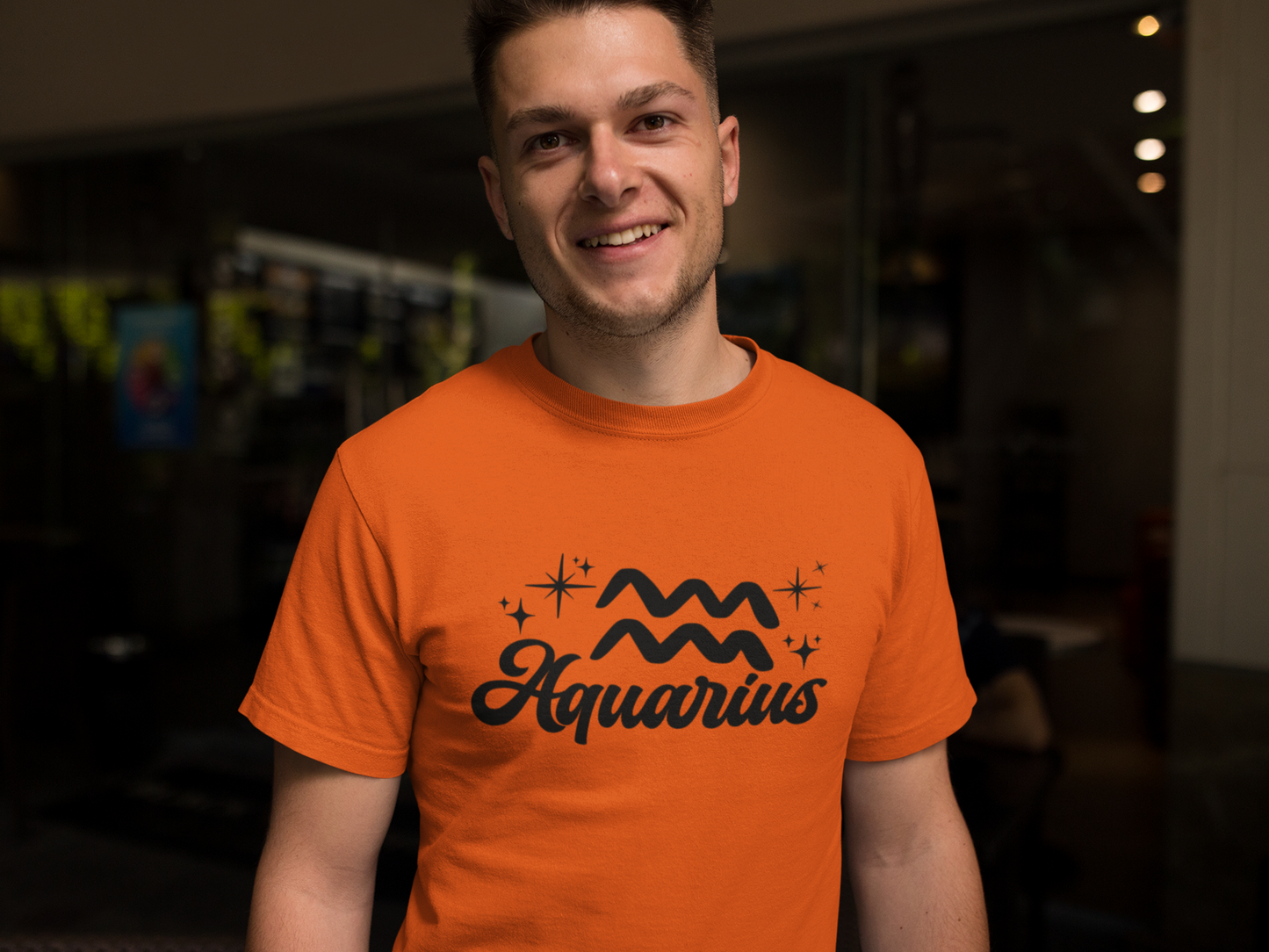Person wearing a orange t-shirt with 'Aquarius' black text design in a dark indoor setting
